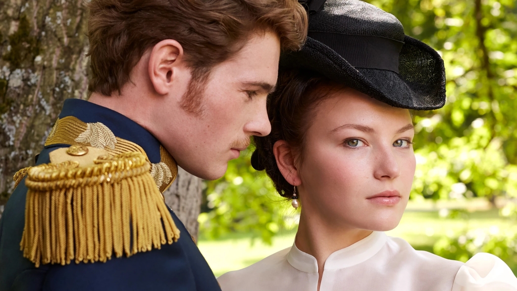 Outdoor image from Netflix series The Empress showing Devrim Lingnau as Sissi in a white blouse, facing the viewer, with Philip Froissant as Franz Joseph in military uniform in profile looking at her.